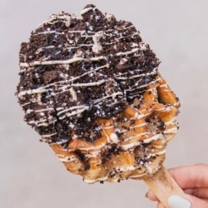 Waffle en paleta cubierto con trozos de galleta Oreo y chocolate blanco derretido. Título: Waffle Oreo Deluxe