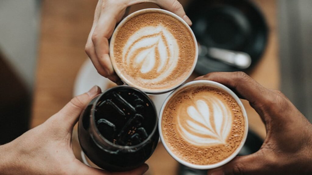 Tres personas sosteniendo bebidas de café, incluyendo latte art y café frío